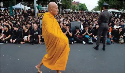  ?? — AFP ?? BANGKOK: A Buddhist monk walks past a large crowd clad in black gathered to pray for the late Thai King Bhumibol Adulyadej outside the Grand Palace.
