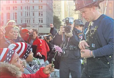  ??  ?? A little girl gives a firefighte­r a flower to place on a makeshift memorial on the site after the attack in New York City on September 11, 2001