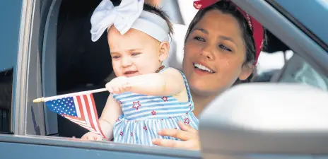  ?? KYLE TELECHAN/POST-TRIBUNE ?? Leighton Humiston, held by her mother, London, waves a flag from the window of a police car during the Griffith Fourth of July parade on Saturday.