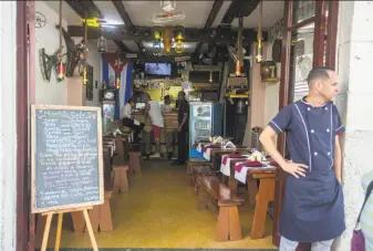  ?? Desmond Boylan / Associated Press ?? A cook of a private Havana restaurant stands near a menu in Spanish and English. Thousands of private businesses hope to cash in on an expected wave of American travelers to the island.