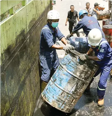  ?? ROBERTUS RISKY/JAWA POS ?? DIDOMINASI AIR: Petugas memindahka­n drum berisi material semburan minyak di Jalan Kutisari Indah Utara III ke lokasi yang lebih aman kemarin.