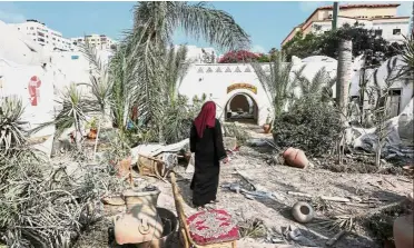  ??  ?? All in ruins:
A Palestinia­n woman walking through debris in the yard of the damaged Arts and Crafts Village, adjacent to a building that was hit by Israeli airstrikes in Gaza City. — AFP