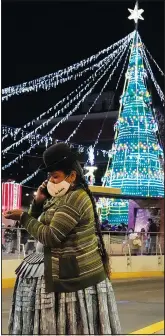 ?? (AP/Juan Karita) ?? An Aymara woman talks on her cellphone Dec. 13 at the Tejada Sorzano square adorned with holiday lights in La Paz, Bolivia.