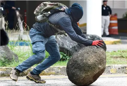  ?? AP FOTO ?? SISYPHUS?
A masked protester rolls a rock during the May Day march in San Juan, Puerto Rico that turned violent. Young protesters clashed with policemen who fired tear gas and rubber bullets when they were hit with stones.