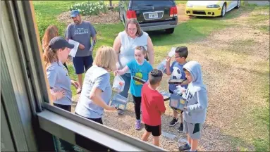  ?? AP-Angie Wang ?? Students receive meals and books from Calhoun City Schools staff and volunteers outside their homes. The school district recently shuttered its doors in an effort to slow the spread of coronaviru­s, but bus drivers still drive their normal routes to deliver hot meals.