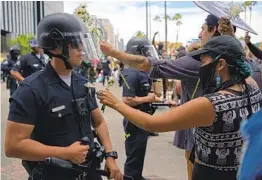  ?? AGUSTIN PAULLIER GETTY IMAGES ?? A protester puts a flower in the pocket of an LAPD officer during a demonstrat­ion Tuesday over the death of George Floyd in Hollywood.