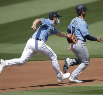  ??  ?? WHO WAS THAT MASKED MAN?: Mariners third baseman Patrick Wisdom (left) applies the tag to Tim Lopes in a rundown during an intrasquad game last week.