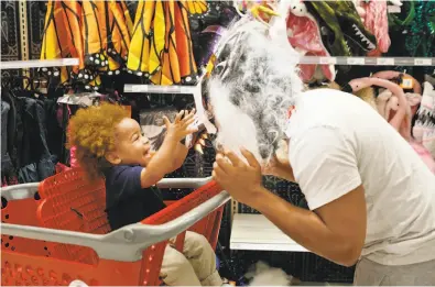  ?? Photos by Brynn Anderson / Associated Press ?? Liam Vasquez, 2, and his father, Will Vasquez, try on Halloween masks at a Target department store in Pembroke Pines, Fla. Discounter­s like Walmart and Target are expanding their costume offerings.