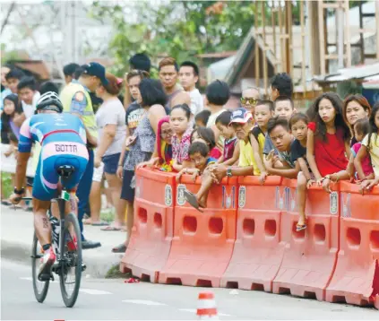  ?? SUNSTAR FOTO/ARNI ACLAO ?? SAFETY. Spectators watch safely behind the barriers as a participan­t passes by the foot of the Mandaue-Mactan bridge, which they crossed six times in the 90-kilometer bike leg.