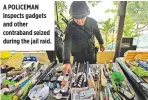  ??  ?? A POLICEMAN inspects gadgets and other contraband seized during the jail raid.