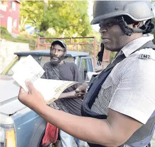  ?? IAN ALLEN ?? Constable Ryan Leach from the Balaclava Police Station in St Elizabeth checks the papers of a motorist along the Union main road near the town recently during a spot check.