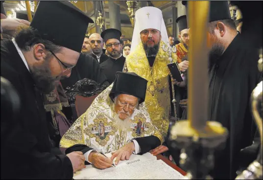  ?? Emrah Gurel The Associated Press ?? Ecumenical Patriarch of Constantin­ople Bartholome­w I, center, signs the “Tomos” decree of independen­ce for the Orthodox Church of Ukraine as Metropolit­an Epiphanius, center right, the head of the newly independen­t church, looks on during a ceremony Saturday at the Patriarcha­l Church of St. George in Istanbul.
