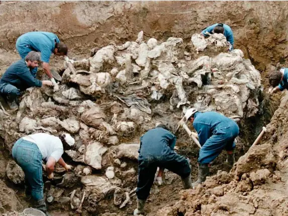  ?? (Getty) ?? Internatio­nal investigat­ors work on top of a cluster of bodies at a mass grave outside the village of Pilica