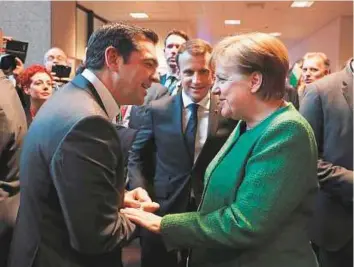  ?? AFP ?? ■ Greek Prime minister Alexis Tsipras (left) greets German chancellor Angela Merkel next to French President Emmanuel Macron (centre) as they meet in a corridor at the end of the European Council meeting in Brussels yesterday.