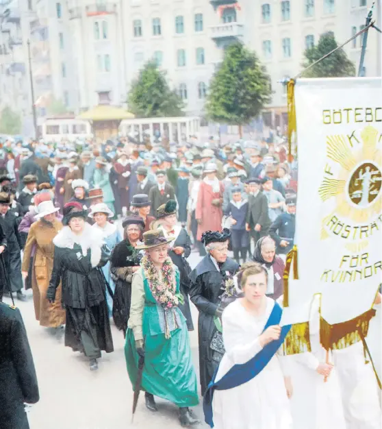  ?? Bild: Hjörnearki­vet ?? Rösträttsd­emonstrati­on i Göteborg den 2 juni 1918. Frigga Carlberg, klädd i svart, är synlig i första ledet efter standarbär­arna. (Bilden är tagen med svartvit film och är färglagd i efterhand av Marina Amaral)