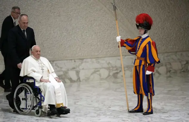  ?? Associated Press photos ?? Pope Francis arrives on a wheelchair at his weekly general audience at the Vatican in February, watched by one of the Swiss Guards.