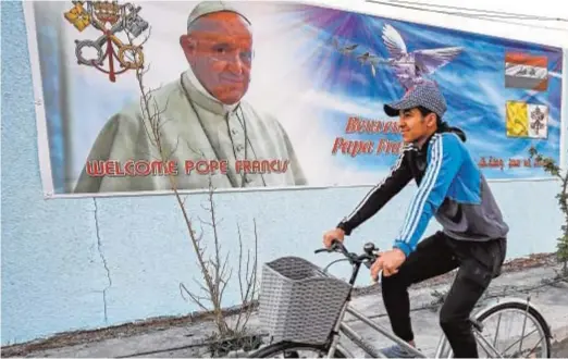  ?? AFP ?? Un joven pasa junto a un cartel de bienvenida a Francisco en una calle de Bagdad (Irak)