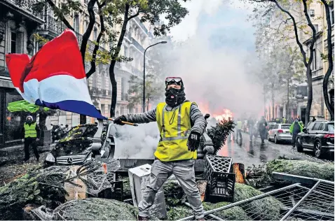  ??  ?? A ‘yellow vest’ protester holds a French flag among a barricade of Christmas trees during a protest against rising petrol taxes and living costs in Paris yesterday. Édouard Philippe, the French prime minister, said that 36,000 people were protesting across France, including 5,500 in the capital, where police made more than 200 arrests.