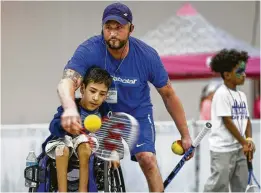  ??  ?? Bourns helps Evan Cruz, 13, with his swing technique as he demonstrat­es wheelchair tennis at Abilities Expo, held in August at NRG Center.