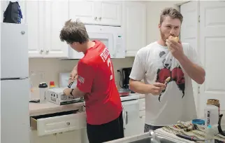  ??  ?? Matt Pare of the single A Augusta GreenJacke­ts, left, opens a box of eggs in the kitchen as teammate Adam Sonabend eats an apple with peanut butter during breakfast in an apartment they share with other teammates.