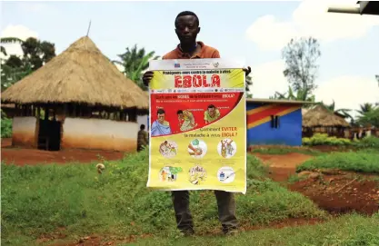  ??  ?? En man i staden Mangina i Kongo-Kinshasa håller upp ett plakat med informatio­n om hur man undviker att smittas av ebola.