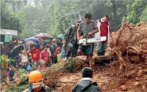  ?? AP ?? Residents and relatives of miners in Itogon township, Benguet province in the northern Philippine­s wait as a worker cuts a toppled tree with a chainsaw as they evacuate following landslides triggered by Typhoon Mangkhut.