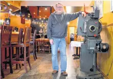  ?? POWELL ?? Capitol Pub owner John Bartlett stands beside a movie projector from 1944 that would have been similar to one used in the Capitol Theatre that opened in 1936 in Middleton. The movie-era relic was given to him by the ZedEx Theatre in Greenwood. LAWRENCE