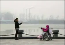  ?? NG HAN GUAN — THE ASSOCIATED PRESS FILE ?? In this file photo taken Saturday visitors to a park gestures at each other near chimneys spewing smoke in Beijing, China.