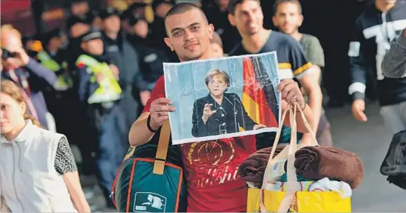  ?? SVEN HOPPE / EFE ?? Un refugiado sirio recién llegado a la estación de ferrocarri­l de la ciudad alemana de Munich exhibe feliz un retrato de la canciller Merkel