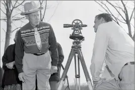  ?? ASSOCIATED PRESS ?? IN THIS APRIL 18, 1958, FILE PHOTO, PHILIP N. BROOKS (right), a New York State surveyor, takes a look through his transit on the Tuscarora Indian Reservatio­n near Niagara Falls, N.Y., while Tuscarora Chief Elton Black Cloud Greene watches. The tribe is resisting state seizure of their land for a power project. In 1959, the U.S. government started the switch from the U.S. survey foot to the internatio­nal foot, and it will finish the job in 2022.