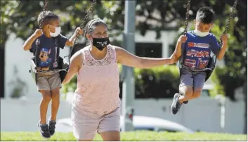  ?? AP photo ?? A woman and two children wear masks at a playground on Saturday in Los Angeles. The number of deaths per day from the coronaviru­s in the U.S. had been falling but now a long-expected upturn has begun, driven by fatalities in states in the South and West.