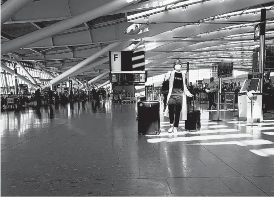  ?? KIRSTY WIGGLESWOR­TH/AP ?? A woman walks through a quiet Heathrow Airport terminal March 24 in London. Air traffic is down 92%, but airlines say rapid virus tests could help.