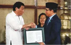  ?? Reuters ?? Rodrigo Duterte presents to Moro Islamic Liberation Front chairman Murad Ebrahim a document containing a signed autonomy law in Manila yesterday.