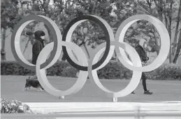  ?? KIICHIRO SATO/AP ?? People wearing a face mask walk by the Olympic rings on Thursday outside Japan Olympic Museum near National Stadium, where the opening ceremony and many other events are planned for postponed Tokyo 2020 Olympics.