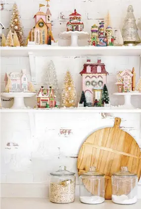  ?? ?? |ABOVE, RIGHT| IT TAKES A VILLAGE. “My Christmas houses comprise one my most treasured holiday collection­s,” Alyssa says. She stages them on cake stands so they have varying heights and can also be easily seen. A dusting of faux snow and a forest of bottlebrus­h trees finish off the shelves.