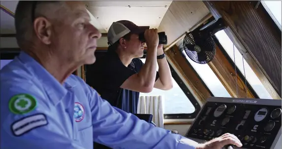  ?? CHARLES KRUPA — THE ASSOCIATED PRESS ?? Aaron Smith, President and CEO of the Offshore Marine Service Associatio­n, center, peers through binoculars at ships installing the South Fork Wind project, as Capt. Rick Spaid, left, pilots the vessel Jones Act Enforcer on July 11, off the coast of Rhode Island.