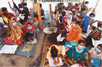  ?? AFP ?? ■ Gypsy children wearing face masks as a preventive measure against the spread of the coronaviru­s attend a tuition class at a slum area in Lahore.