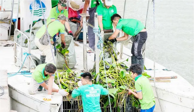  ?? PHOTOGRAPH BY KING RODRIGUEZ FOR THE DAILY TRIBUNE ?? RIVER patrollers of the Department of Environmen­t and Natural Resources clear hyacinths obstructin­g the stream along William A. Jones Memorial Bridge.