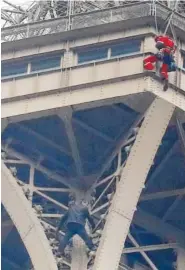  ?? AP PHOTO/ MICHEL EULER ?? A rescue worker, top in red, hangs from the Eiffel Tower while a climber is seen below him between two iron columns Monday in Paris. The Eiffel Tower was closed to visitors after the person tried to scale it.