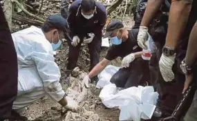  ?? PIC BY EIZAIRI SHAMSUDIN ?? Forensic officers examining remains found in a grave near an abandoned migrant camp at Bukit Wang Burma, near the PerlisThai border.