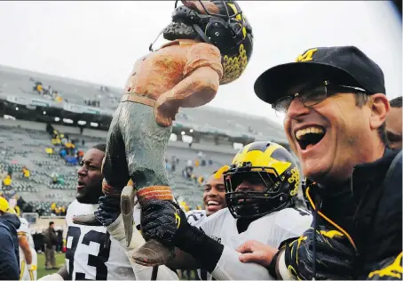  ?? CARLOS OSORIO/THE ASSOCIATED PRESS ?? Members of the Michigan Wolverines including coach Jim Harbaugh, right, walk off the field with the Paul Bunyan Trophy after beating state rival Michigan State Spartans 21-7 in East Lansing, Mich, on the weekend.