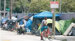  ?? JOE BURBANK/ORLANDO SENTINEL ?? A cyclist talks to a pedestrian near a tent row outside the Coalition for the Homeless in downtown Orlando on July 31.