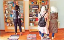  ??  ?? Two women look at books while a volunteer, left, organizes books at the 'Baynetna' cultural centre library in Berlin.