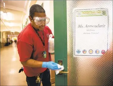  ?? Photograph­s by Francine Orr Los Angeles Times ?? TRACY WESTFIELD cleans a door handle at L.A.’s John Burroughs Middle School as a precaution against the coronaviru­s. California school officials are ordering hand sanitizers while designing contingenc­y plans.