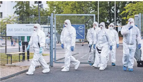  ?? FOTO: DPA ?? Beamte der Polizei und des Ordnungsam­tes in Schutzanzü­gen vor einer Flüchtling­sunterkunf­t in St. Augustin.