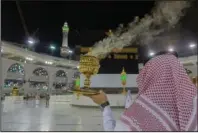  ?? The Associated Press ?? HAJJ: A man burns incense as the area around the Kaaba, the square structure in the Great Mosque, toward which believers turn when praying, is prepared for pilgrims, in Mecca, Saudi Arabia, late Sunday. Anywhere from 1,000 to 10,000 pilgrims will be allowed to perform the annual hajj pilgrimage this year due to the virus pandemic.