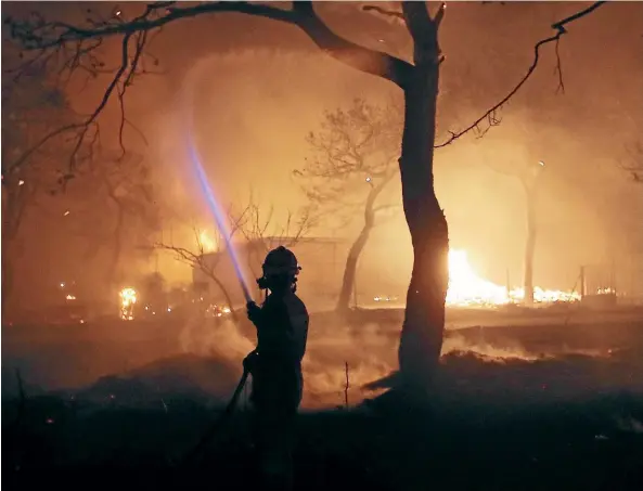  ?? AP ?? A firefighte­r sprays water on the fire in the town of Mati, east of Athens. Regional authoritie­s have declared a state of emergency in the eastern and western parts of the greater Athens area as fires fanned by gale-force winds raged through pine...