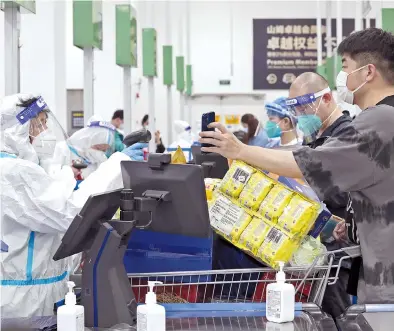  ?? — Xinhua ?? Customers pay for the goods at a Sam’s Club outlet in the Pudong New Area. Some retailers in Shanghai have reopened their stores, with manufactur­ers resuming production.