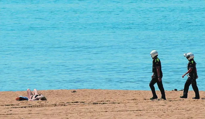  ?? EFE ?? Agentes de la Guardia Urbana se dirigen a una persona que estaba tomando el sol en una playa de Barcelona