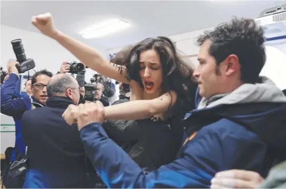  ?? Picture: LUCA BRUNO ?? A topless female protester is carried away from a polling station where Italian former premier and leader of the Forza Italia (Go Italy) party Silvio Berlusconi was about to vote. More than 46 million Italians were voting on Sunday in the general...